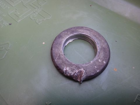 1993 Ford Taurus - A close-up view of a worn and damaged metal washer on a textured green surface.