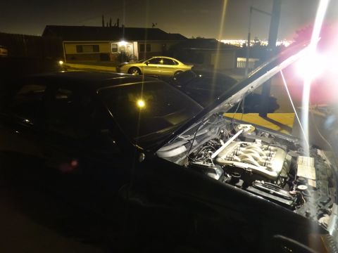 1993 Ford Taurus - Engine bay of a 1993 Ford Taurus is visible with the hood up at night, another car in background.