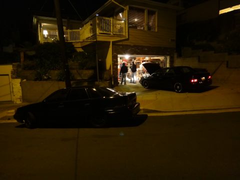 1993 Ford Taurus - Two black sedans are parked outside a house at night, one with its hood open.