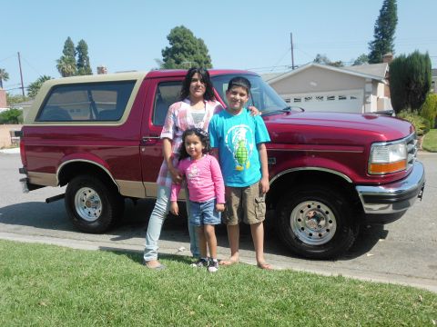 1994 Ford Bronco - A family poses in front of a red and tan Ford Bronco SUV parked on a suburban street.