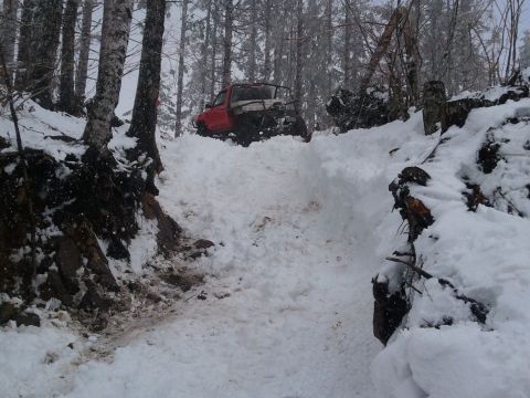 1994 Ford Bronco - A red off-road vehicle navigates a challenging snowy terrain in a forest.