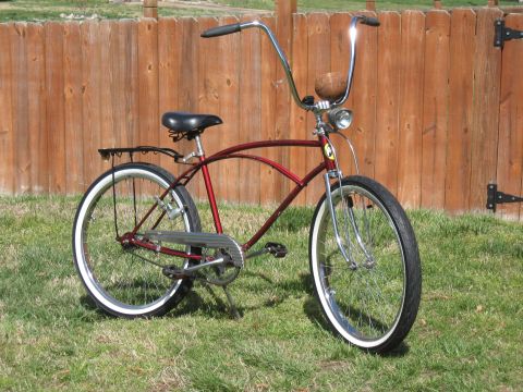 1994 Ford Bronco - A red cruiser bicycle with whitewall tires is parked on grass in front of a wooden fence.