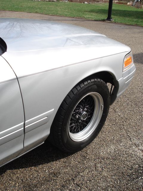 2000 Ford Crown Victoria - Front fender and wheel of a silver 2000 Ford Crown Victoria black wire-spoke wheels.