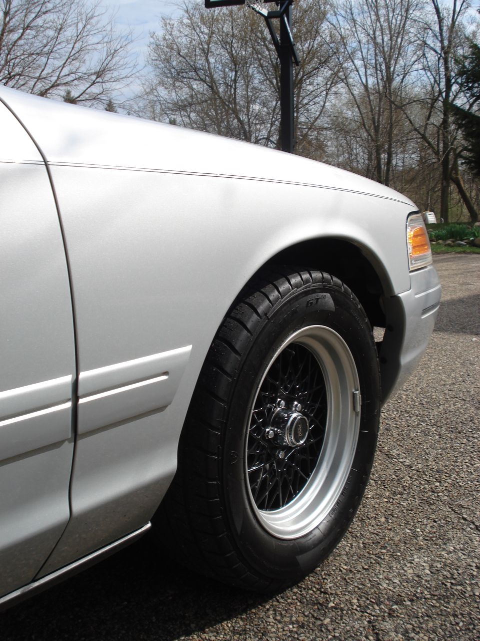 Silver 2000 Ford Crown Victoria fender and wire-spoke wheel with black spokes and polished lip