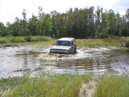 1991 Ford Bronco - A Ford Bronco navigates a water obstacle in a wooded area.