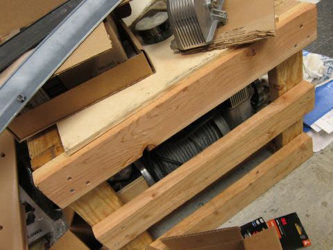 1987 Dodge 1500 - A winch and its steel cable are stored on a wooden pallet, with various boxes and metal pieces around it.