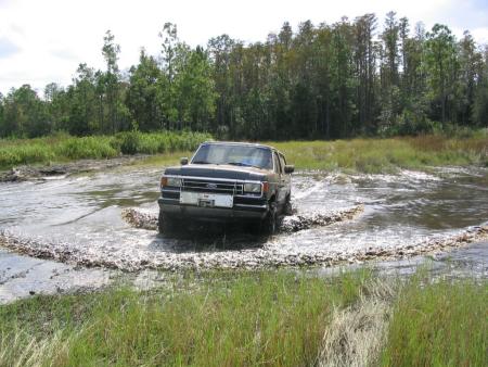 1991 Ford Bronco - A black 1991 Ford Bronco navigates a watery, off-road terrain.