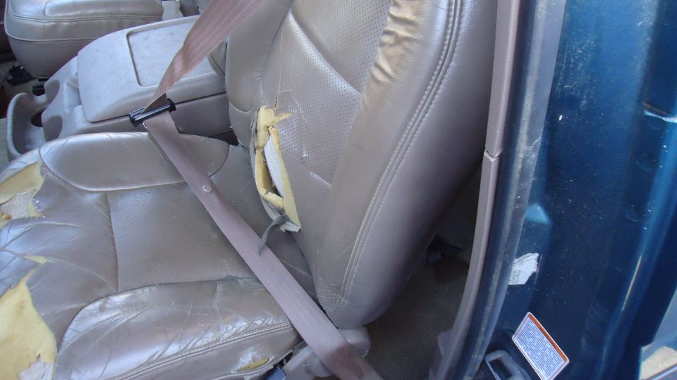 Interior view of a torn leather car seat with a seatbelt. The foam is exposed
