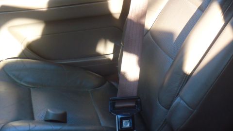 1996 Ford Bronco - The interior of a vehicle shows a perforated leather seat and a brown seatbelt.