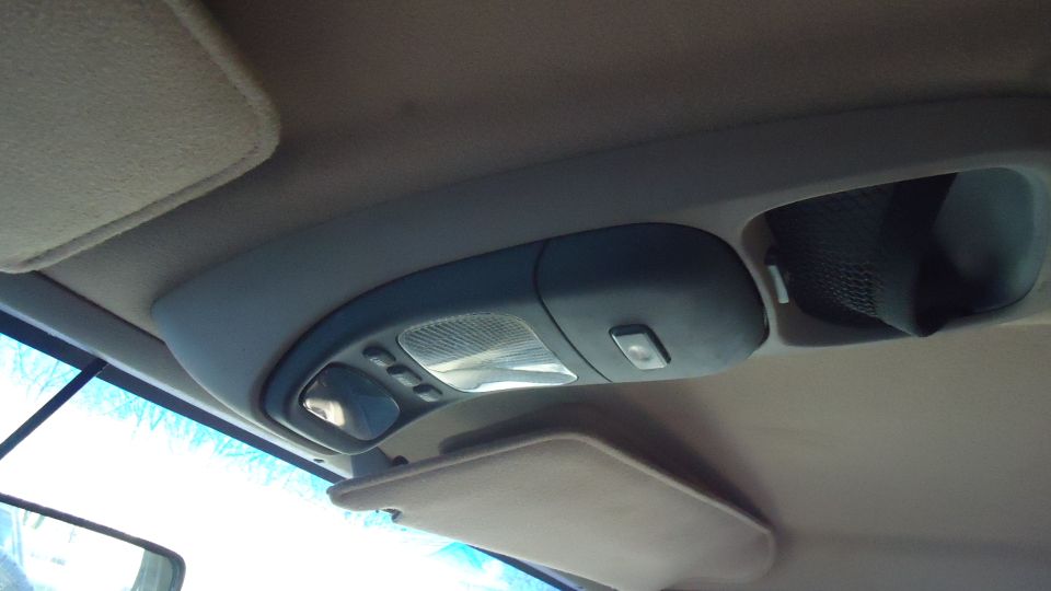 Interior shot of a vehicle's overhead console, showing lights, buttons, and a small mirror
