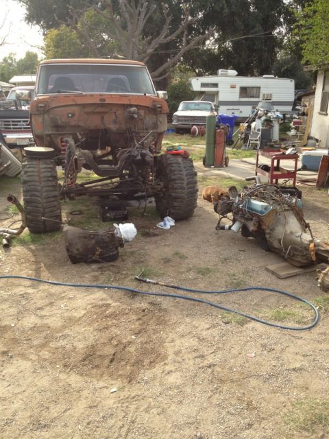 1969 Ford F-250 - Pickup truck chassis sits in a yard, stripped of its engine and transmission, with parts laid out nearby.