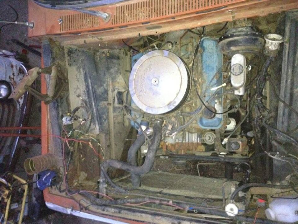 Engine bay showing a V8 engine with air cleaner, brake booster, and wiring. Part of an orange vehicle is visible