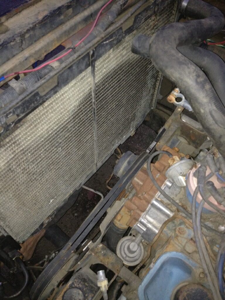 Close-up of a vehicle's engine bay, showing the radiator, hoses, belts, and engine block