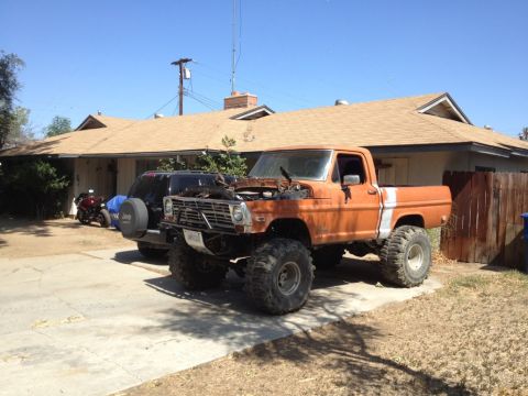 1969 Ford F-250 - This lifted 1969 Ford F-250 pickup truck is parked in a driveway with its hood open, revealing the engine.