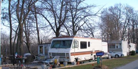 1997 Ford Taurus - An RV and a white sedan are parked in a lot with trees and mobile homes in the background.