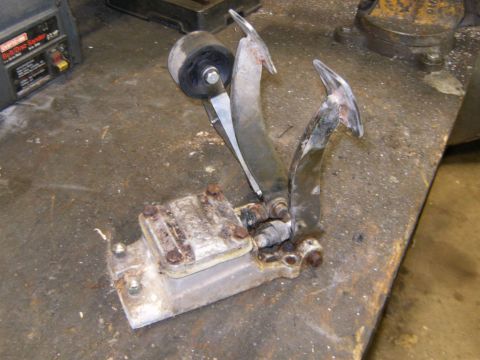 2000 Ford E350 - A worn brake and clutch pedal assembly sits on a cluttered workbench, showing signs of rust and use.