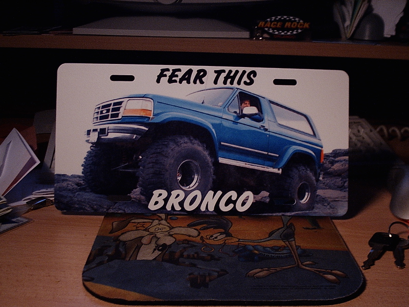 Novelty license plate of a lifted blue Ford Bronco reading 'FEAR THIS BRONCO'