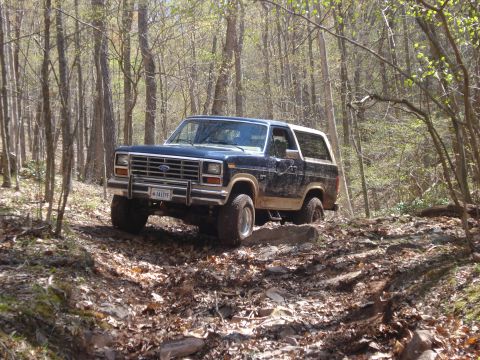 1985 Ford Bronco - This Ford Bronco navigates a rocky, wooded trail, kicking up dirt as it goes.