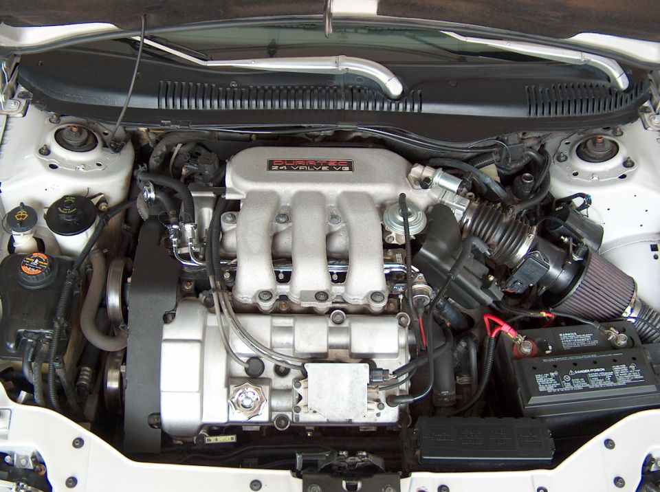 Engine bay of a transverse 24-valve V6 with a red cone air filter in a white car