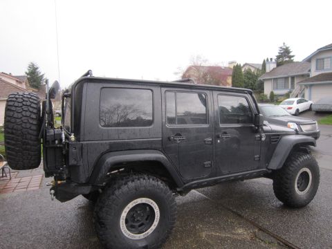 2008 Jeep Wrangler - black lifted four-door Jeep Wrangler on large mud tires with a rear bumper tire carrier, parked in a driveway.