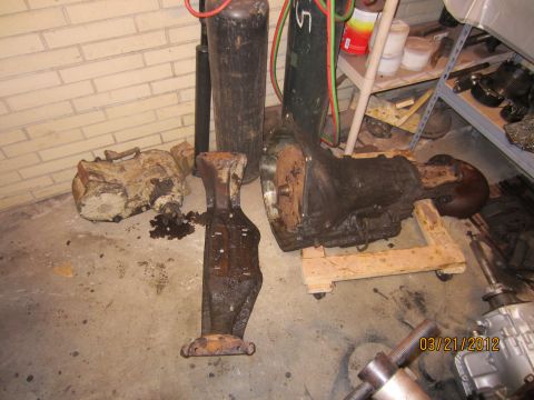1979 Ford Bronco - Multiple rusty drivetrain components are laid out on the floor, possibly awaiting repair or replacement.