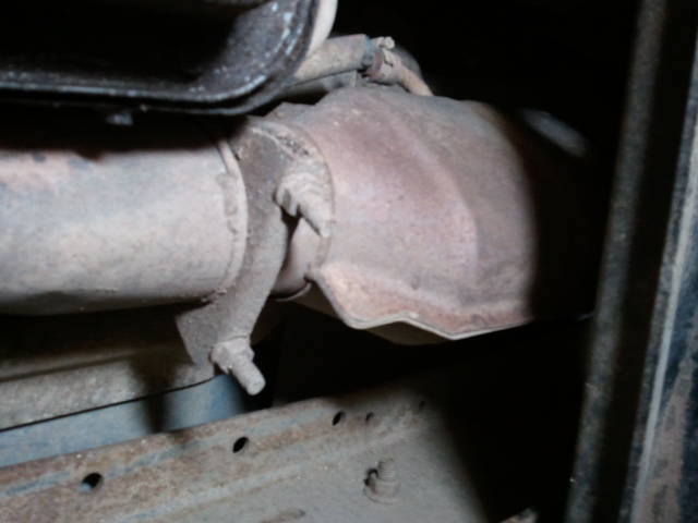 Rusty exhaust pipe, clamp, and muffler seen from underneath a vehicle