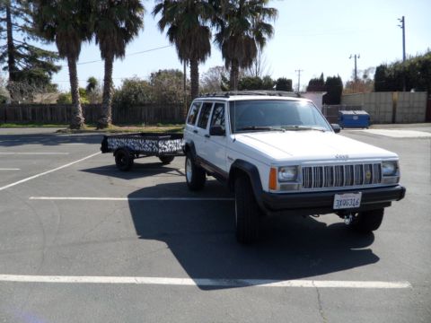 1994 Jeep Cherokee - White 1994 Jeep Cherokee parked in a lot, towing a small trailer with a distinctive pattern.