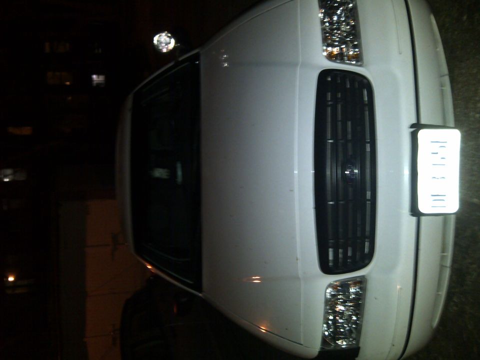 Front view of a white sedan with a black grille and headlights. A light is mounted on the roof