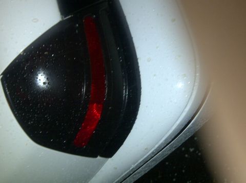 2000 Ford Crown Victoria - Water droplets cover the rear quarter panel and a blacked-out taillight of a white car.