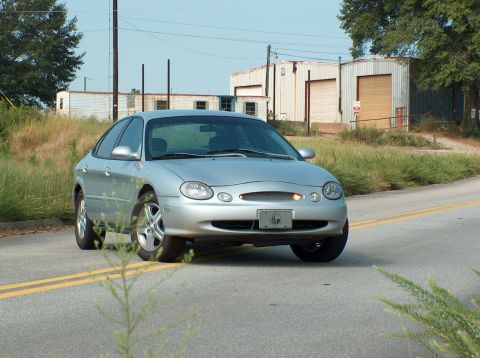1998 Ford Taurus - A silver sedan is parked on a road with industrial buildings in the background.