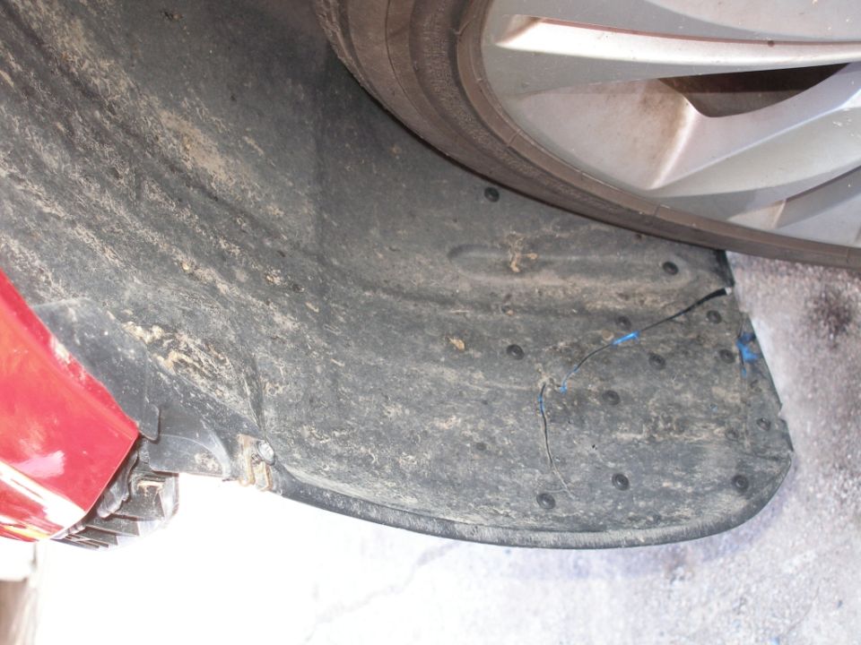 Close-up of a dirty wheel well liner with a tire visible above. Some blue tape is on the liner