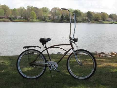 1994 Ford Bronco - A maroon cruiser bicycle with tall handlebars is parked on the grass next to a lake.