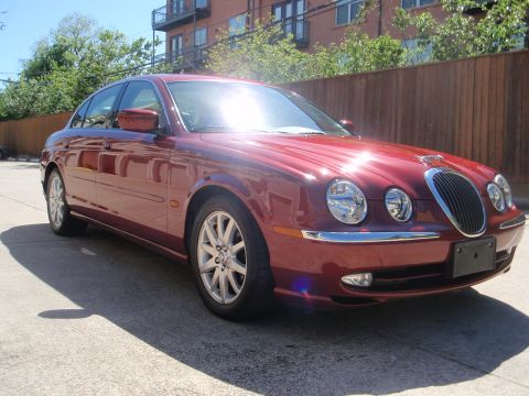 2000 Jaguar S-Type - A red 2000 Jaguar S-Type sedan is parked outdoors on a sunny day, showing its distinctive grille and headlights.