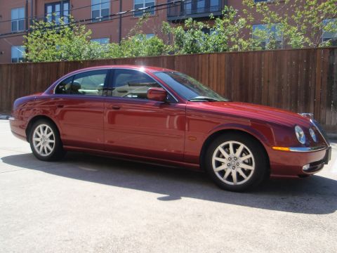 2000 Jaguar S-Type - A red sedan is parked on a concrete surface with a wooden fence and building in the background.