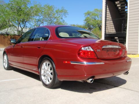 2000 Jaguar S-Type - Rear view of a red 2000 Jaguar S-Type sedan parked on pavement near a building.