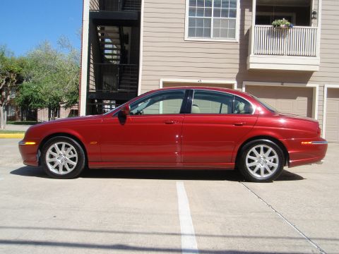 2000 Jaguar S-Type - Side profile of a red 2000 Jaguar S-Type sedan parked in front of a tan building.