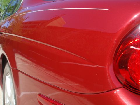 2000 Jaguar S-Type - Close-up of a red sedan's rear quarter panel, showing a pinstripe detail and minor imperfections.