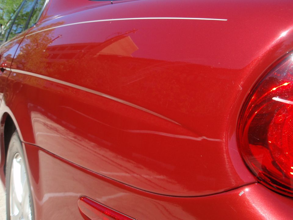 Red sedan's rear quarter panel with a pinstripe and some scratches. Tail light visible