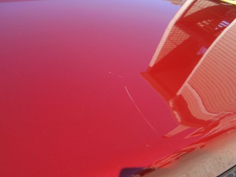 2000 Jaguar S-Type - A scratch mars the otherwise glossy red paint on a car's hood, with a building reflected in the surface.