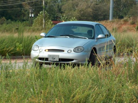 1998 Ford Taurus - A silver sedan is parked in overgrown grass, viewed from the front.