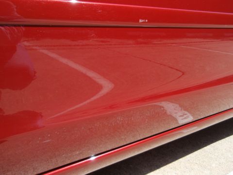 2000 Jaguar S-Type - Close-up of a red car's side panel, showing reflections and surface imperfections.
