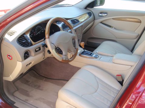 2000 Jaguar S-Type - The interior of a red Jaguar S-Type features tan leather seats, a wood-trimmed steering wheel, and a center console with a gear shifter.