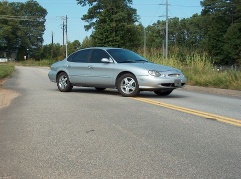 1998 Ford Taurus - A silver sedan is captured from a three-quarter front view as it travels down a two-lane road.