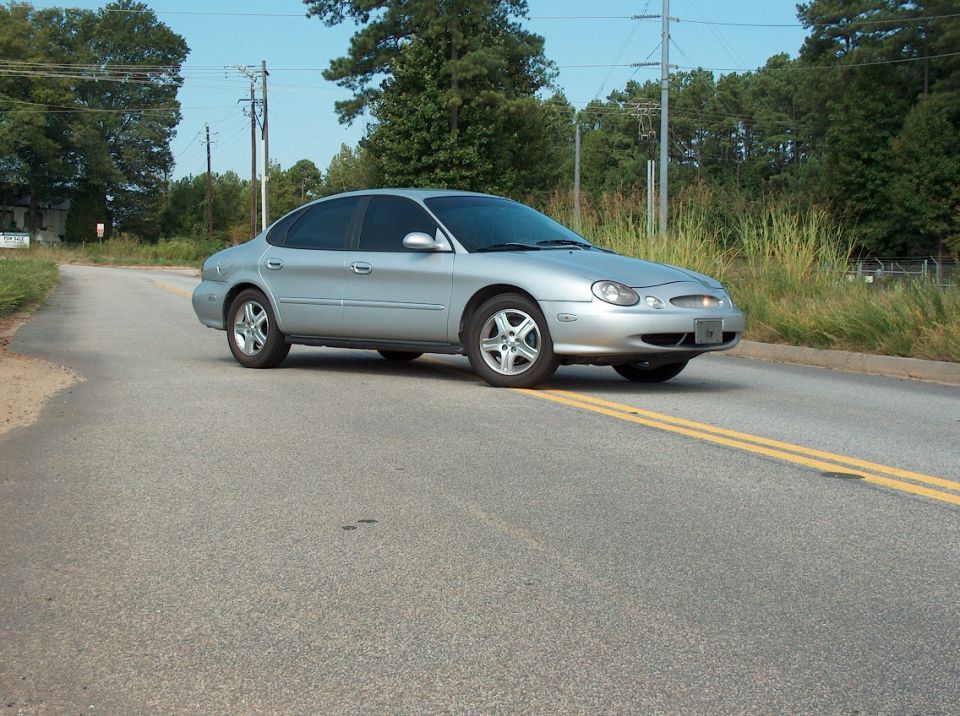 Silver sedan with tinted windows driving on a paved road with double yellow lines