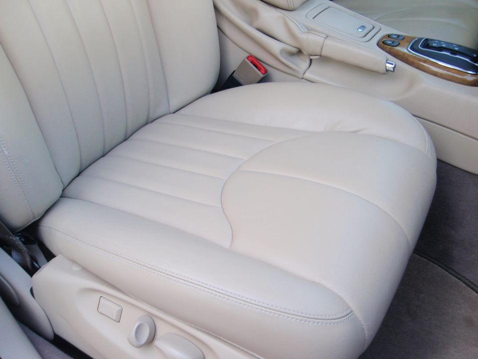 Beige leather car seat with stitching, seat adjustment controls, and part of the center console visible