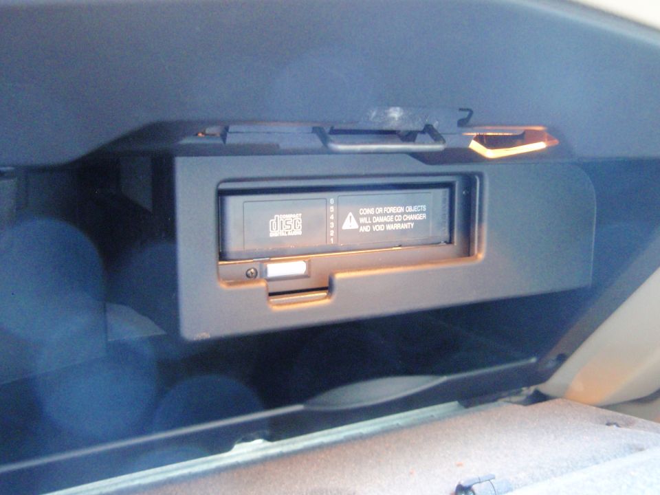 Car's CD changer unit inside a compartment, with warning text about foreign objects