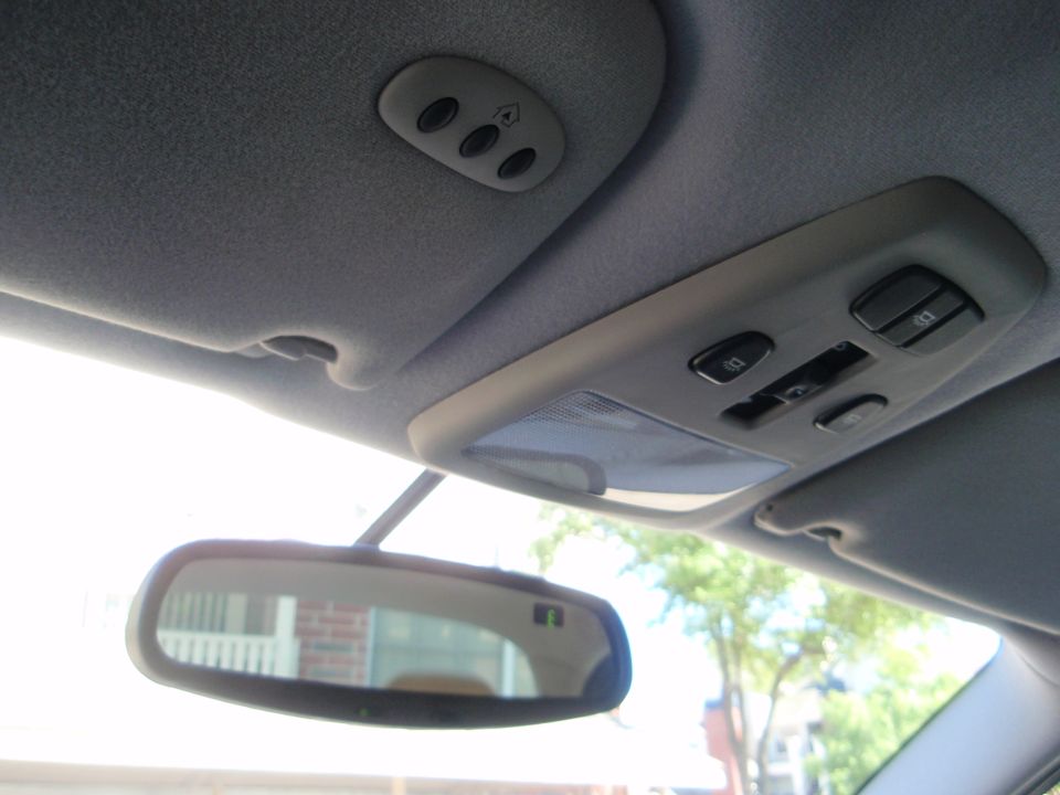 Interior view of a car's ceiling console with garage door openers and a rearview mirror reflecting a building