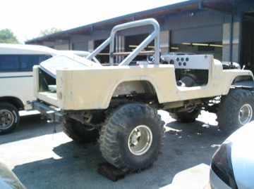 1978 Ford Bronco - A yellow off-road vehicle is parked outside a building, showing its modified body and large tires.