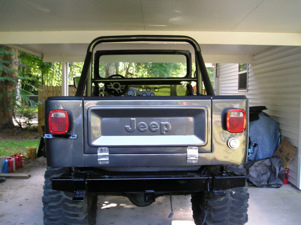 Rear view of a gray Jeep CJ-7 with a roll cage, spare tire carrier, and aftermarket bumper