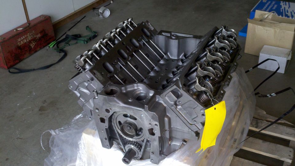 Engine block with valve covers and timing chain visible, yellow tag attached